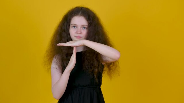 Portrait of a young tired and bored girl doing a timeout gesture isolated on yellow background