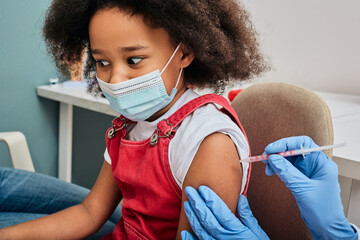 African American female child during vaccination in doctor's office. Vaccination of children while...