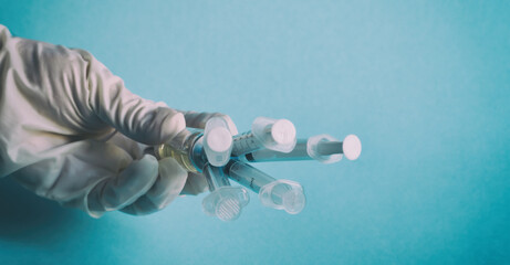 The doctor's hand in a white glove holding a vial of vaccine, which protrude from five syringes....