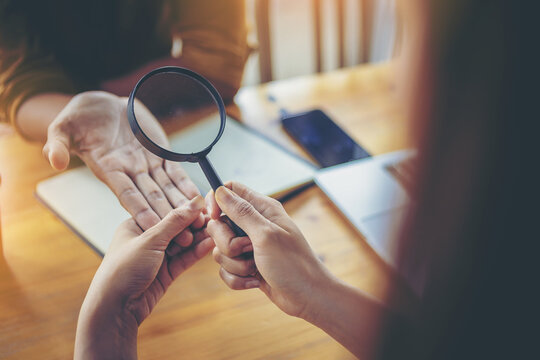 A woman seer is watching horoscope for her colleague. The young woman shining a magnifying glass to colleague in office.