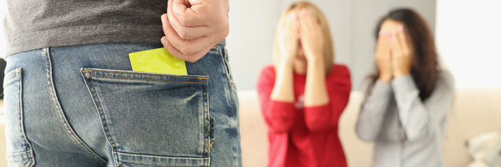 Man takes condom out of his jeans pocket, two women are sitting opposite and covering their eyes...
