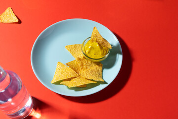 Nachos chips with cheese sauce on blue plate on red background. Mexican food photo