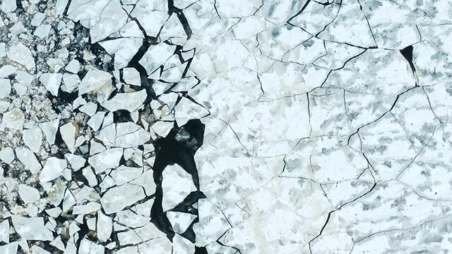 Aerial fly over view of cracked ice floes floating in the sea. Dark water as background. Beautiful pattern. Large densely dispersed pieces. Forward camera movement. 4k footage.