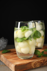 Tasty melon ball drink on wooden table against black background
