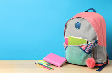 Stylish backpack and different school stationery on wooden table against light blue background,...