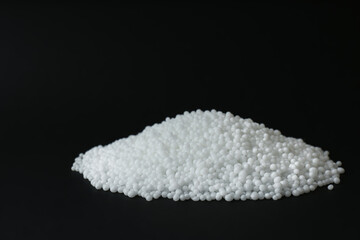 Pellets of ammonium nitrate on black background, space for text. Mineral fertilizer
