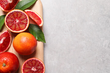 Ripe red oranges, green leaves and wooden board on light table, top view. Space for text