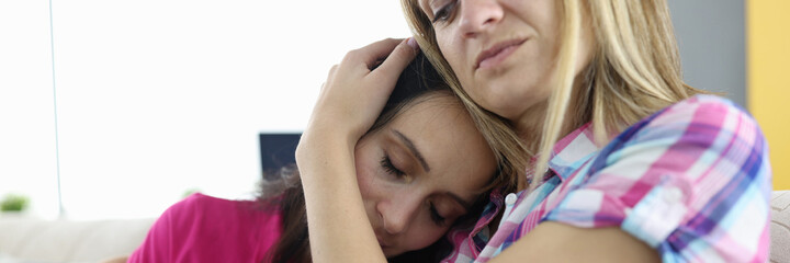 Young woman lies on shoulder of her friend and cries with an ovulation test in her hand. Unwanted...