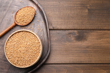 Mustard seeds with bowl and spoon on wooden table, flat lay. Space for text