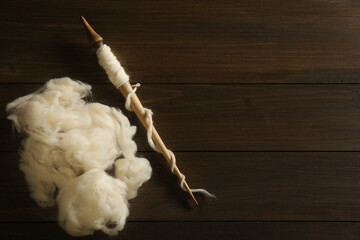 Soft white wool with spindle on wooden table, flat lay. Space for text