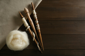 Soft white wool with spindles on wooden table, flat lay. Space for text
