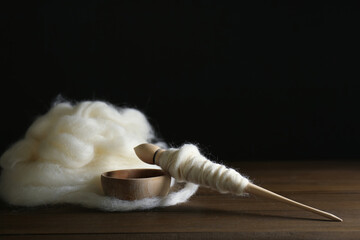 Fototapeta na wymiar Soft white wool and spindle on wooden table against black background, space for text