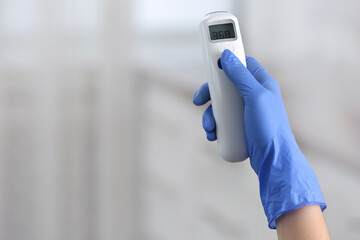 Closeup view of doctor with infrared thermometer on blurred background, space for text. Checking temperature during Covid-19 pandemic