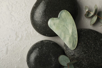 Jade gua sha tool, spa stones and eucalyptus branches on grey table, flat lay © New Africa