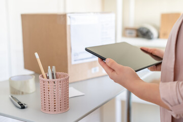 Woman with tablet at workplace of start up, small business owner. Cardboard parcel box of product...