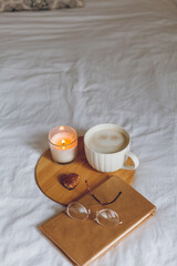 Breakfast in bed. Coffee mug, heart-shaped cookies, book, glasses, candle, wooden tray. Women's Day. Cozy.