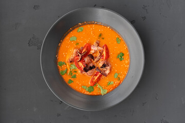 Tom yam Thai soup in black bowl served on gray background
