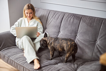 Bulldog smelling a woman with laptop on bed