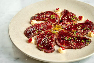 Japanese classic dish - tataki beef with unagi sauce, hot pepper, served in a beige plate on a marble background. Restaurant food