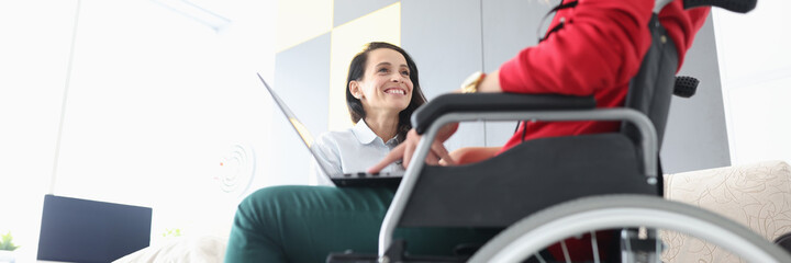 Disabled woman in wheelchair communicates with smiling friend with laptop on her lap. Psychological...