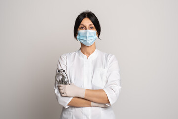 Female doctor or scientist wearing protective facial mask standing with crossed arms over grey background