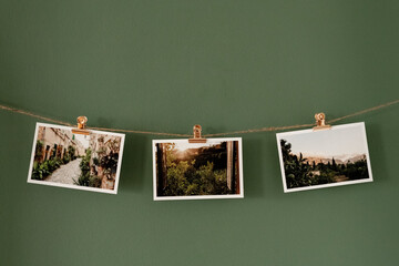 Postkarten mit Landschaftsmotiven an einer Schnur hängend vor einer grünen Wand, roséfarbene Klammern.