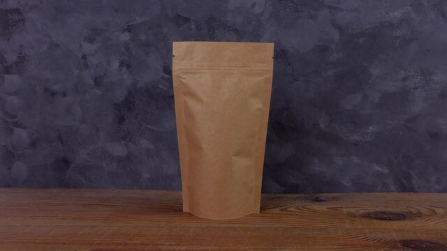 Hand in rubber gloves holds brown paper pouch bags mockup with coffee beans shows thumb up like wooden background Packaging food delivery goods template.Kraft pack with clasp tea leaves weight product