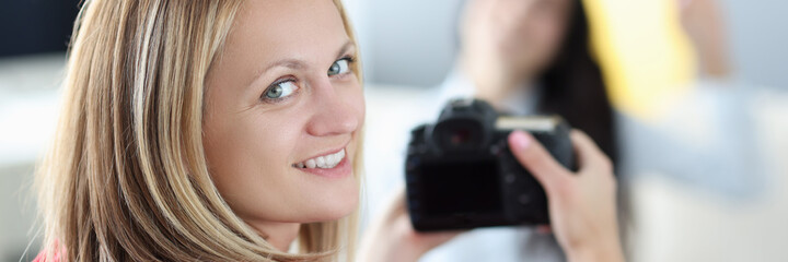 Young woman photographer holding camera in her hands with brunette in background at home. Passion for photography hobby concept.