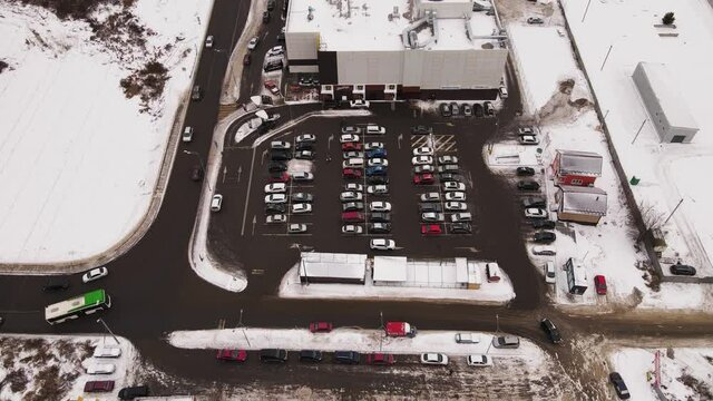 Cars move and stand in even rows in a line in the parking lot. Bird's eye view of a large number of cars. The vehicles are next to the mall, the owners are gone shopping.