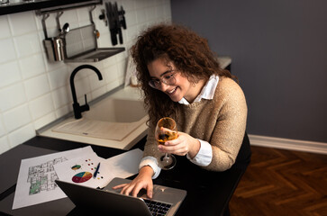Portrait of young woman working at home in kitchen using laptop.	