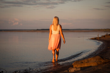 Fototapeta na wymiar blonde girl on the riverbank at sunset, selective focus