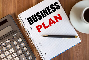 BUSINESS PLAN written in a white notepad near a calculator and a cup of coffee on a dark wooden background