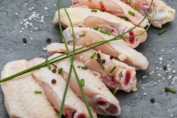 Close-up of raw chicken wings marinated with salt, pepper and chives on a black slate board. © PhotoStk