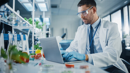 Male Scientist Working on a Laptop Computer, Creating Lab-Grown Food for Vegetarians. Microbiologist Working on Molecule Samples in Modern Laboratory with Technological Equipment.