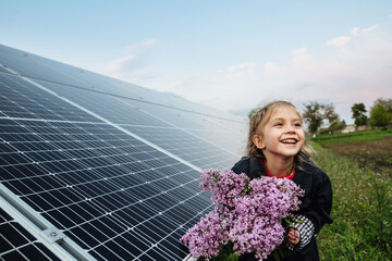 A child with a future of alternative energy and sustainable energy. The child holds flowers on a background of solar panels, photovoltaic. Environmental friendliness and clean energy concept.