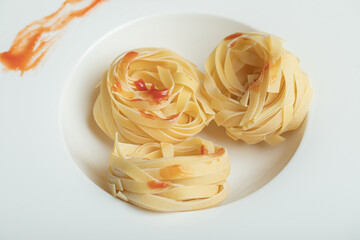 A white plate of uncooked nest noodles with red pepper