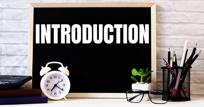 The word INTRODUCTION is written on the chalkboard next to the white alarm clock, glasses, potted plant, and pencils in a stand.