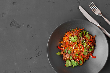 Top view of wok noodles with vegetables and meat in bowl on gray background