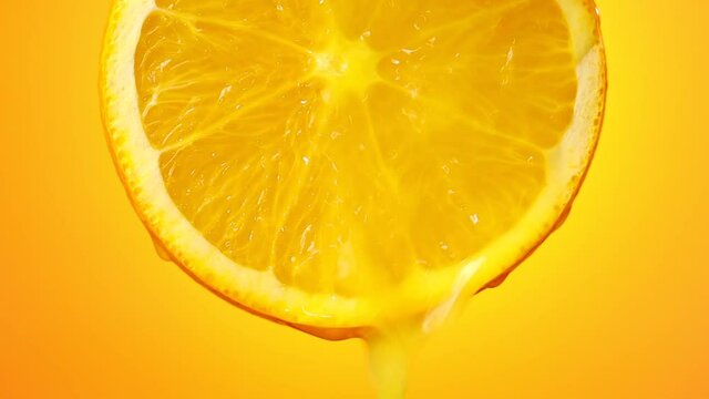 freshly squeezed orange juice flows from the ripe fruit slice close - up on a orange background