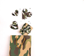 Khaki shopping bag with gift box and camouflage hearts on white background. Defender of the Fatherland Day, February 23. Space for text.