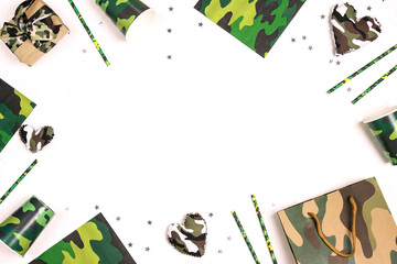 Party set with camouflage glasses, straws, napkins and gifts on white background with copy space for text.