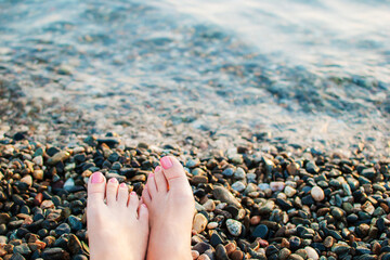women's legs with pink manicure relax on the beach on wet pebbles