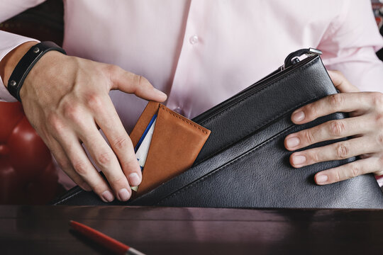 A Business Man Puts A Leather Wallet With Credit Cards In His Briefcase. Closeup, No Face