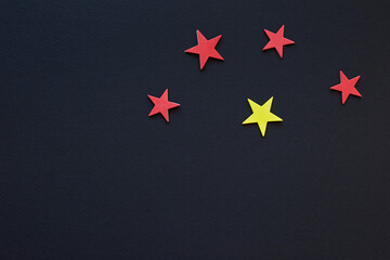 Four red paper stars and single yellow star on dark background; 5 star color design; flag type; top view, flat lay