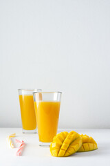 Mango juice in glasses with juice and a straw on a white background, chopped mango and whole, delicious healthy sweet natural drink