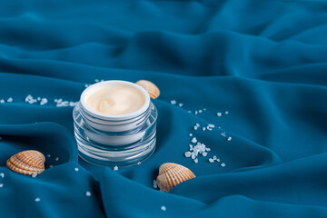 mineral moisturizer cream, shells, sea ​​salt  in glass jar, blue background draped cloth....