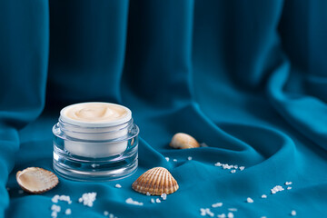 mineral moisturizer cream, shells, sea ​​salt  in glass jar, blue background draped cloth....