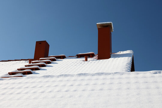The roof with a chimney is covered with snow in winter