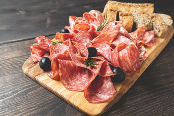 Sliced salumi salami on a wooden board with olives and multigrain baguette. italian food, appetizer for aperitif or salami sandwich. Top view