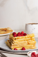 Stack golden pancakes or crepes with raspberries in a grey plate and coffee. Breakfast concept. Maslenitsa.
